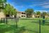 Charming apartment complex surrounded by lush greenery with a spacious fenced yard under a vibrant blue sky.