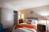 Cozy bedroom featuring a stylish upholstered bed, vibrant pillows, and a warm orange throw, complemented by elegant furniture and soft lighting.