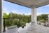 Chic balcony with modern white wicker chairs and table, offering serene views of lush green trees and a clear blue sky.