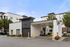 Modern apartment complex entrance with elegant white and gray facade, featuring lush green landscaping and convenient drive-through access.