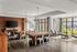Modern communal living space featuring sleek wooden tables, industrial-style chairs, and stylish light fixtures set against a backdrop of floor-to-ceiling windows.