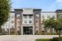 Contemporary apartment building with modern architecture, featuring sleek brick and panel facade, lush landscaping, and ample parking space.
