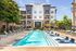 Luxurious apartment complex with a sparkling outdoor pool, elegant lounge chairs, and vibrant green landscaping.