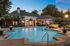 Elegant community pool area at sunset featuring a luxurious clubhouse, cozy lounge chairs, and lush landscaping.