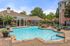 Luxurious community pool area with elegant brick architecture, surrounded by lush greenery and comfortable lounge chairs.