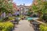 Charming apartment complex with a lush garden pathway leading to a serene pool area, surrounded by blooming pink trees and stylish seating.