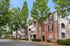 Charming brick apartment complex with inviting balconies and lush trees lining a quiet street, perfect for serene living.