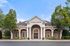 Charming leasing center with elegant brick fa&ccedil;ade, classic columns, and lush green surroundings under a bright blue sky.