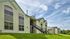 Charming apartment exterior with modern siding, large windows, and lush green landscape under a bright blue sky.
