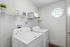 Bright laundry room with modern washer and dryer, featuring elegant shelving and a charming octagonal window.