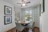 Charming dining nook with round wooden table, patterned chairs, and scenic window view.