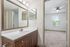 Chic bathroom with modern wooden vanity and large mirror, adjacent to a bright bedroom featuring plush carpeting and a picturesque window view.