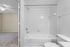 Bright and modern bathroom with a pristine white bathtub and elegant tile design, adjacent to a cozy carpeted bedroom.