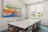 Elegant dining room with a modern white table, colorful chairs, and vibrant landscape painting.