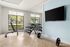 Modern home gym with large windows, workout bench, dumbbells, and a wall-mounted TV.