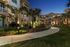 Beautifully landscaped apartment complex with vibrant garden and palm trees, lit by elegant pathway lighting at dusk.