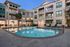 Evening view of a modern apartment complex with a sparkling swimming pool, surrounded by lounge chairs and elegant balconies.