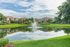 Scenic apartment complex with stunning lake view, lush greenery, and elegant architecture under a blue sky.