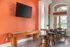 Inviting entertainment area with bright orange accent wall, a large wall-mounted TV, shuffleboard table, and elegant wooden bar seating, perfect for relaxation and gatherings.