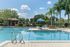 Inviting outdoor pool area with lush landscaping, cozy seating under a blue umbrella, and clear skies promising relaxation and leisure.