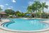Inviting outdoor swimming pool in a luxurious apartment complex with lush palm trees and sunlit lounging area.