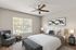 Bright and modern bedroom with elegant decor, featuring a stylish ceiling fan, cozy seating nook by a large window, and tasteful artwork on the wall.