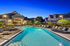 Elegant apartment complex with sparkling swimming pool, surrounded by lush greenery and stylish lounge chairs under a serene evening sky.