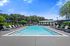 Luxurious outdoor swimming pool area with comfortable lounge chairs, blue umbrellas, and lush greenery under a vibrant blue sky.