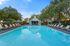 Inviting outdoor pool area with luxurious sun loungers and vibrant umbrellas, surrounded by lush greenery and a charming pool house.