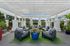 Chic outdoor patio featuring plush seating under a stylish white pergola, surrounded by lush greenery and vibrant potted plants.