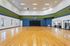 Modern indoor basketball court with polished wooden flooring and colorful walls, adjacent to a fitness center.