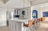 Contemporary kitchen with sleek white cabinetry, vibrant blue backsplash, and stylish pendant lighting. Spacious seating area with brown leather barstools and open access to a chic living space.