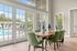 Bright dining area with green chairs and wooden table, overlooking a sparkling pool through elegant French doors.