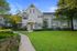 Charming two-story townhouse with elegant facade, surrounded by lush greenery and vibrant flowers under a clear blue sky.