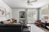 Bright and elegant living room with large windows, contemporary furniture, and tasteful decorative accents. Cozy gray sofa, stylish armchairs, and abstract art create a welcoming ambiance.