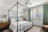 Elegant bedroom with a canopy bed, modern decor, and a large window framed by green curtains, creating a serene ambiance.