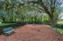 Charming dog park with agility equipment, surrounded by lush greenery and shaded by large trees.