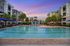 Luxurious apartment complex showcasing a stunning pool area surrounded by palm trees and modern architecture at sunset.