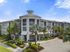 Modern luxury apartment building with elegant architecture surrounded by lush palm trees under a bright blue sky.