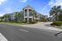 Luxurious modern apartment complex surrounded by lush palm trees and vibrant landscaping, set against a clear blue sky.