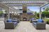 Inviting outdoor patio featuring cozy wicker furniture with blue cushions, a charming stone fireplace, and lush greenery under a stylish pergola.
