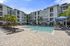 Luxurious apartment complex with modern design featuring a spacious pool area, surrounded by lush palm trees, elegant lounge chairs, and shaded umbrellas.