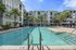 Modern apartment complex with a luxurious pool surrounded by palm trees and spacious lounging areas under blue umbrellas.