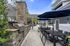 Charming outdoor patio with stone grill, dining set under blue umbrellas, and lush greenery, perfect for entertaining.