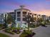 Elegant apartment building at sunset with lush landscaping and modern design, featuring illuminated entryways and palm trees.