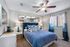 Elegant bedroom with a cozy blue bed, stylish patterned pillows, modern lamps, and natural light through large windows.
