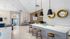 Modern communal kitchen area with sleek white countertops, stylish pendant lighting, and cozy seating. Warm wood accents and contemporary artwork create an inviting atmosphere.