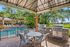 Inviting outdoor barbecue area with modern grills and dining set adjacent to a refreshing swimming pool surrounded by lush greenery.