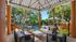 Inviting outdoor sitting area with stylish wicker furniture, vibrant pillows, and a picturesque view of lush greenery and a sparkling pool.