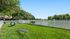 Charming green park with well-kept grass, white picket fence, and serene water views, perfect for relaxation and outdoor activities.